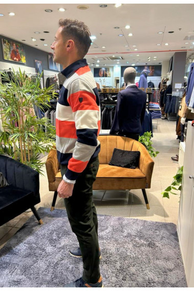 Homme de profil portant le polo manches longues orange à rayures. Col chemise et coupe classique.