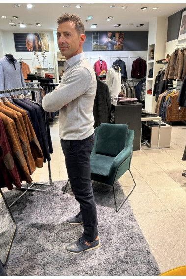 Homme de profil portant le pull col V gris clair avec une chemise. Coupe regular.