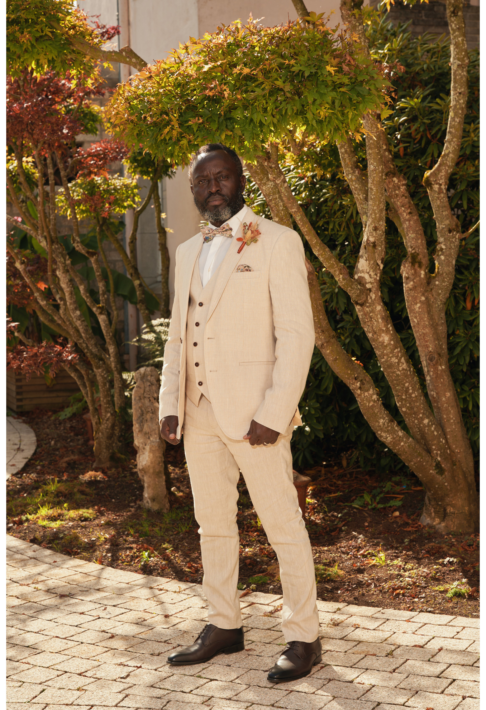 Homme en position trois-quarts en costume GIORGIOC couleur beige 3 pièces dans une cours.