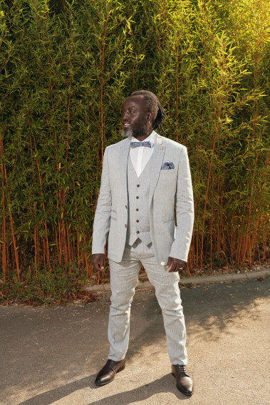 Homme de face en costume GIORGIO couleur bleu clair 3 pièces dans une cours. Il porte des chaussures marrons.