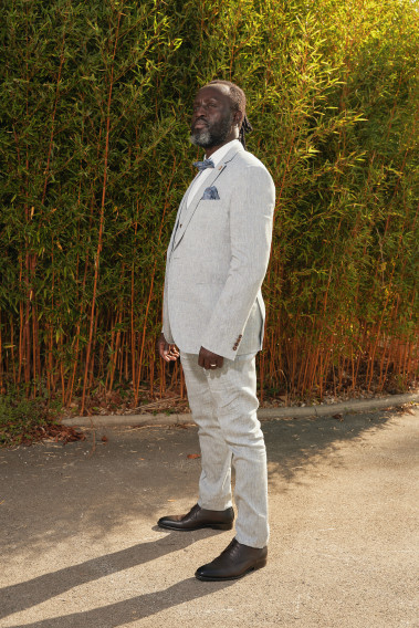 Homme de profil en costume GIORGIO couleur bleu clair 3 pièces dans une cours. Il porte des chaussures marrons.