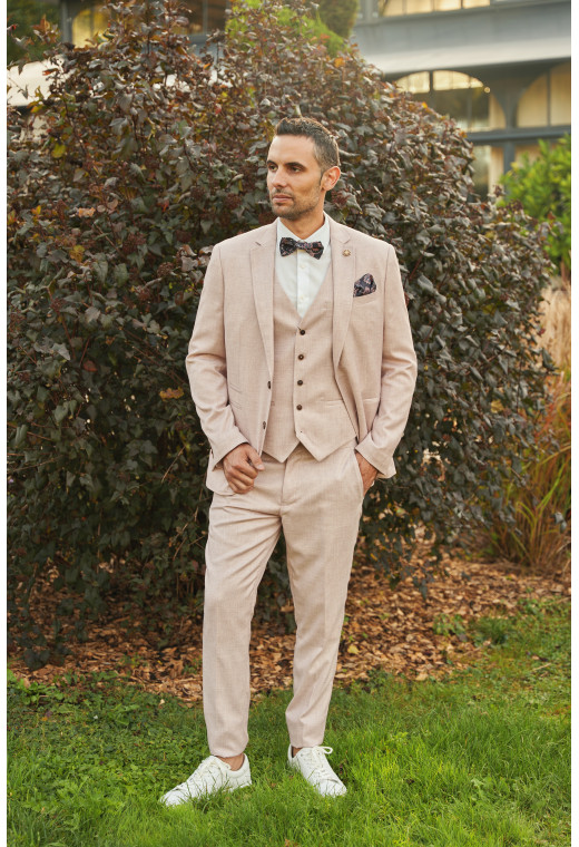 Homme de face en costume GIORGIO couleur rose pâle 3 pièces dans une cours. Il porte des baskets blanches.