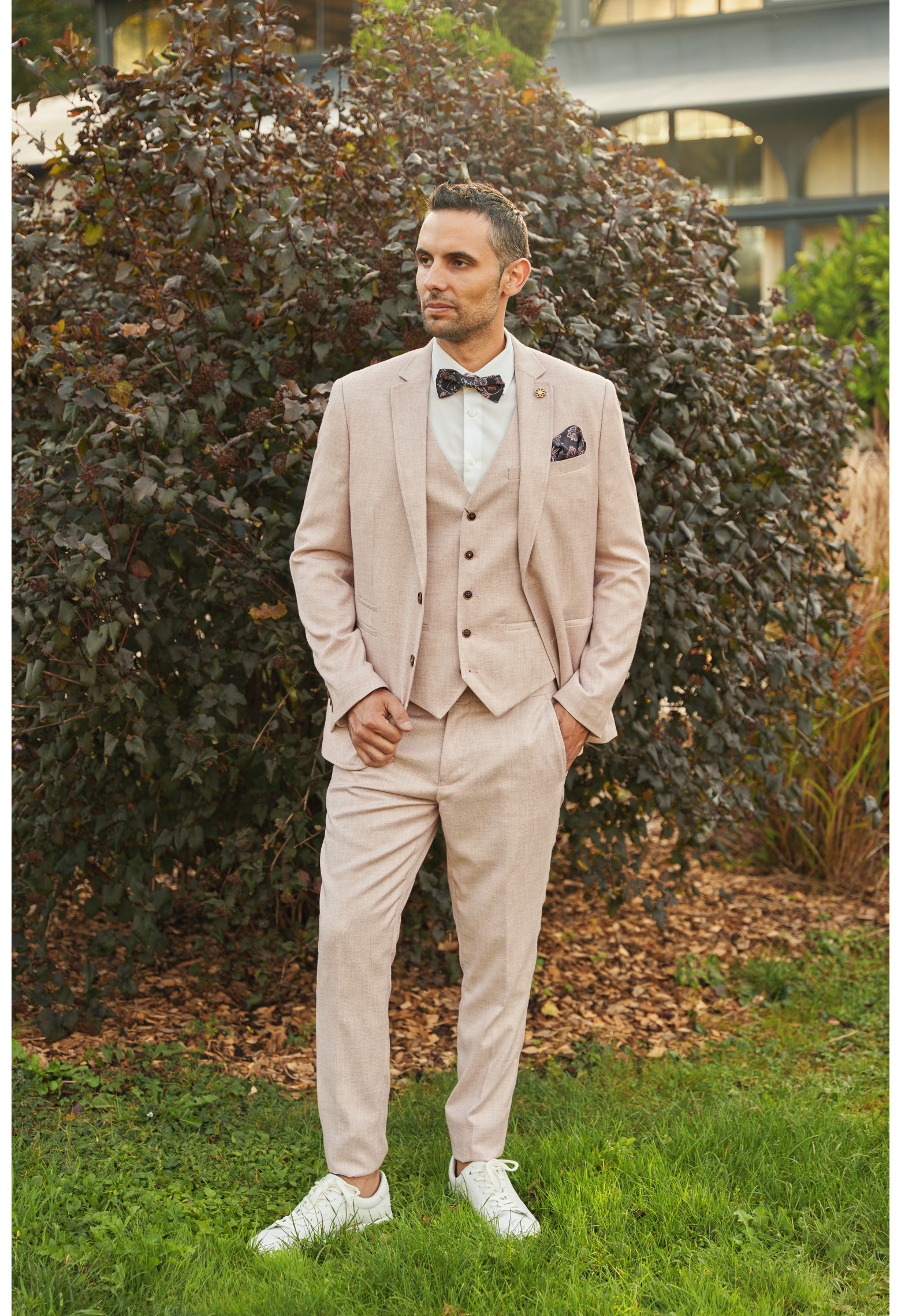 Homme de face en costume GIORGIO couleur rose pâle 3 pièces dans une cours. Il porte des baskets blanches.