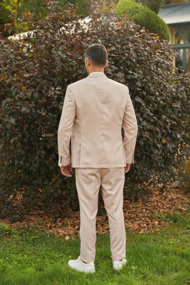 Homme de dos en costume GIORGIO couleur rose pâle 3 pièces dans une cours. Il porte des baskets blanches.