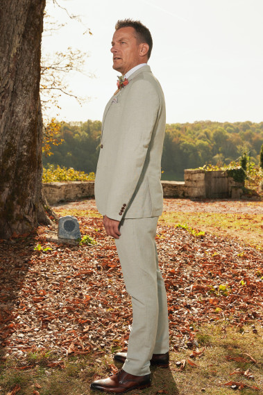 Homme de profil en costume GIORGIO couleur vert 3 pièces devant un arbre. Il porte un pins bouquet de fleur.