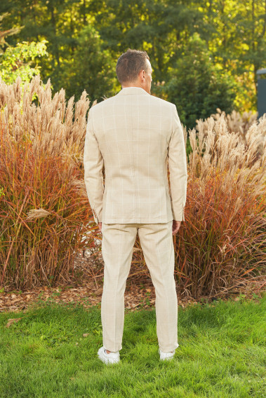 Homme de dos en costume GIORGIOC couleur beige à carreaux dans une cours. Il porte des baskets blanches.