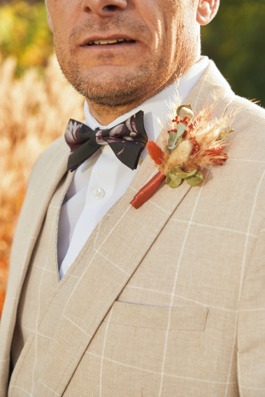 Zoom sur costume GIORGIOC beige à carreaux avec noeud papillon noir et mauve et pins bouquet de fleur.