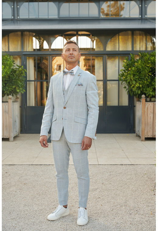 Homme de face en  costume GIORGIOC couleur bleu à carreaux 3 pièces devant une maison.