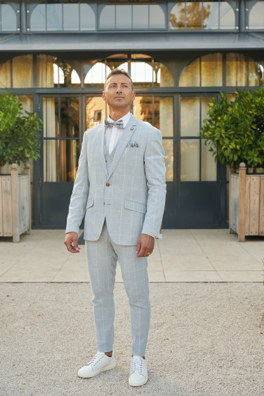Homme de face en  costume GIORGIOC couleur bleu à carreaux 3 pièces devant une maison.