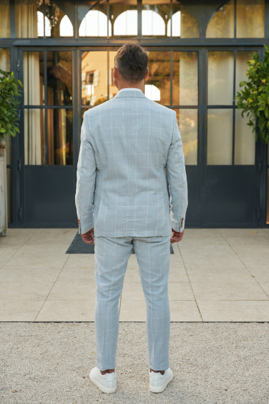 Homme de dos en  costume GIORGIOC couleur bleu à carreaux 3 pièces devant une maison.