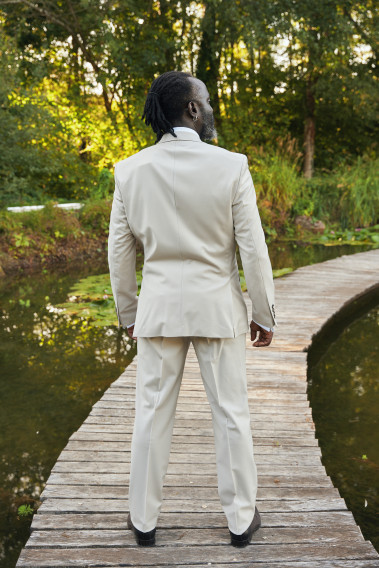 Homme de dos en costume SUAT couleur craie sur un pont dans un lac. Il porte des chaussures marrons.