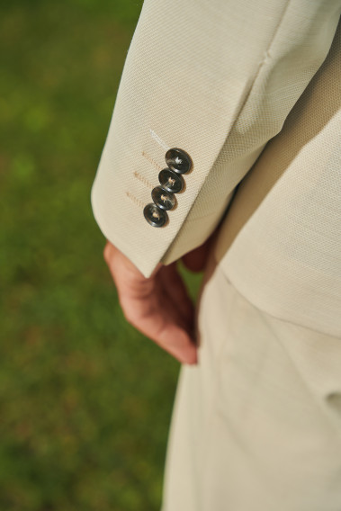 Zoom sur la manche du costume SUAT couleur beige. Elle comporte 4 boutons marrons.