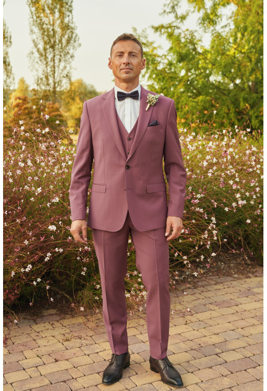 Homme de face en costume SUAT couleur fushia 3 pièces dans une cours fleurie.