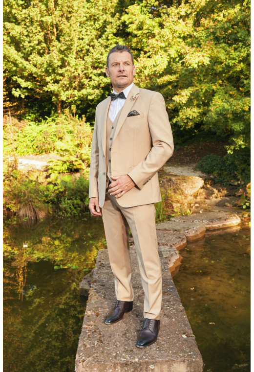 Homme en position trois-quarts en costume SUAT couleur beige sable 3 pièces sur un pont dans un lac.