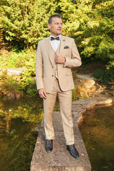 Homme de face en costume SUAT couleur beige sable 3 pièces sur un pont dans un lac.