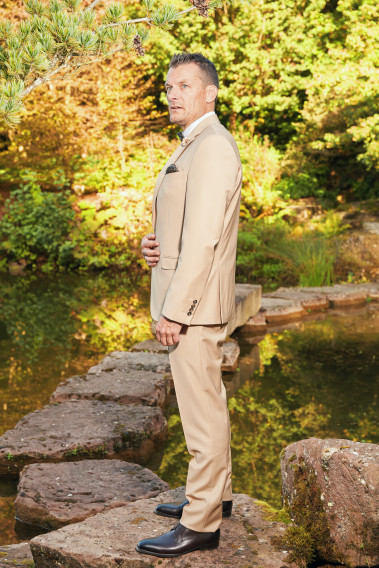 Homme de profil en costume SUAT couleur beige sable 3 pièces sur un pont dans un lac.