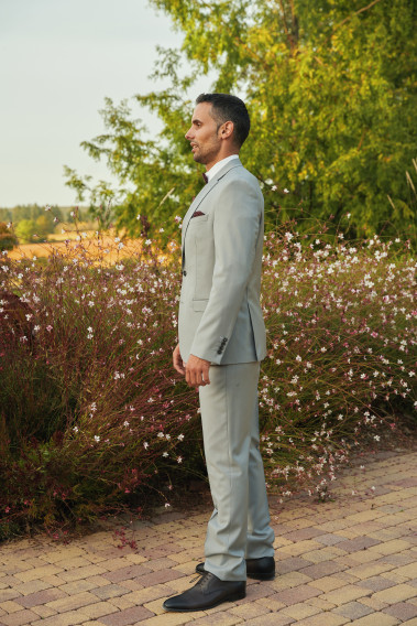 Homme de face en costume SUAT gris clair 3 pièces dans  une cours. Il porte des chaussures marrons.