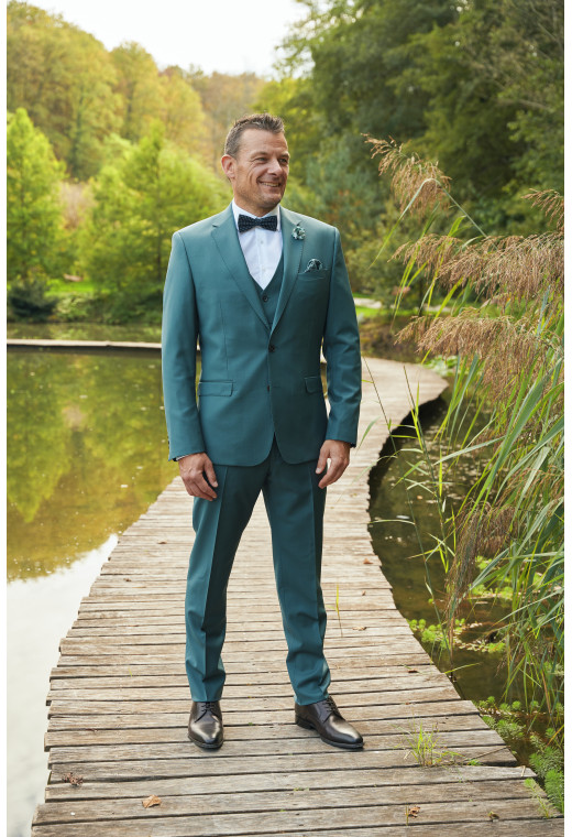 Homme de face en costume SUAT couleur vert bleuté 3 pièces sur un pont dans un lac.