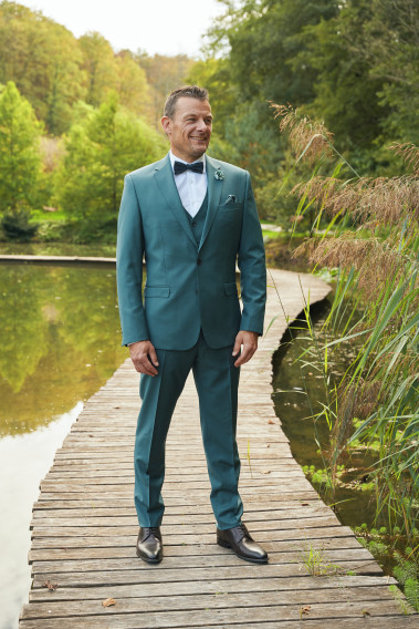 Homme de face en costume SUAT couleur vert bleuté 3 pièces sur un pont dans un lac.