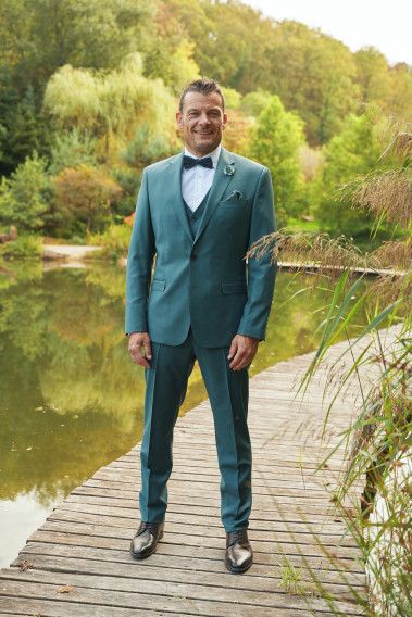 Homme de face en costume SUAT couleur vert bleuté 3 pièces sur un pont dans un lac.