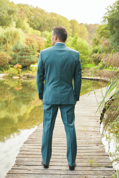 Homme de dos en costume SUAT couleur vert bleuté sur un pont dans un lac.