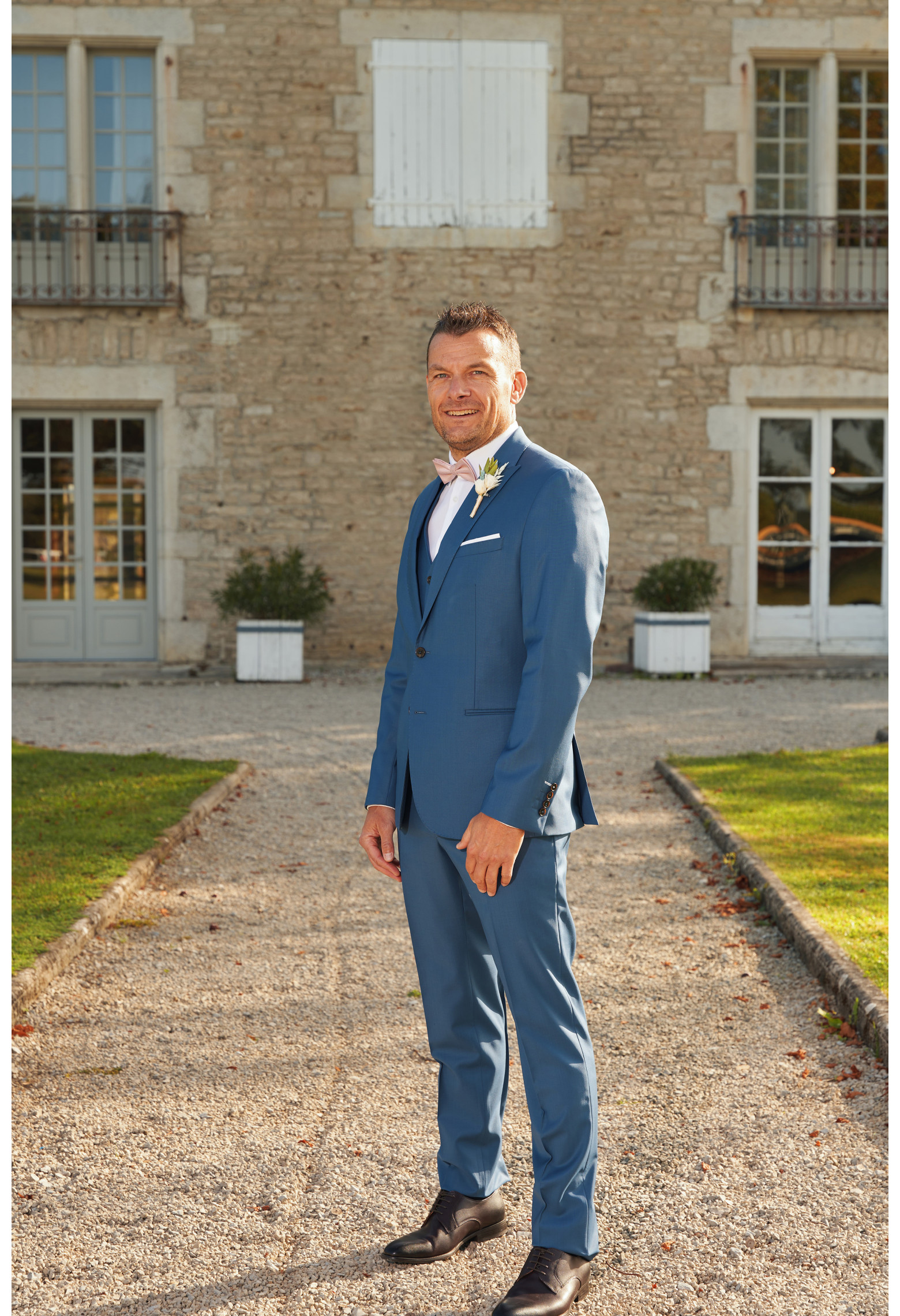 Homme en position trois-quarts en costume SUAT couleur bleu devant une maison.