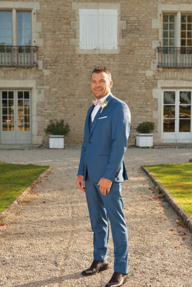 Homme en position trois-quarts en costume SUAT couleur bleu devant une maison.