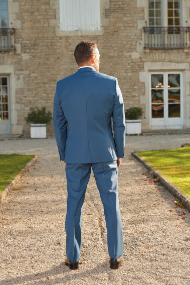 Homme de dos en costume SUAT couleur bleu devant une maison.