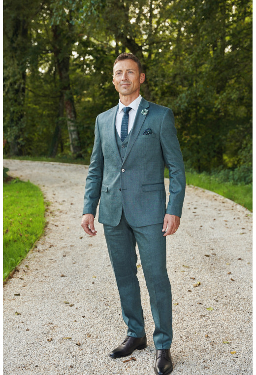 Homme de face en costume SUAT couleur vert 3 pièces dans une cours.
