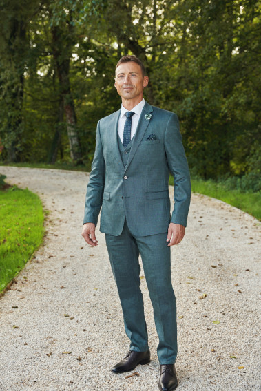 Homme de face en costume SUAT couleur vert 3 pièces dans une cours.