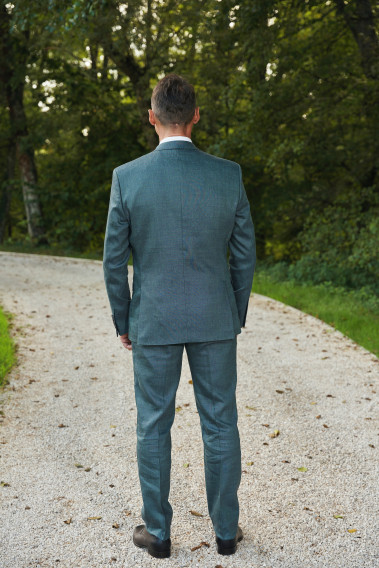 Homme de dos en costume SUAT couleur vert dans une cours. Il porte des chaussures marrons.