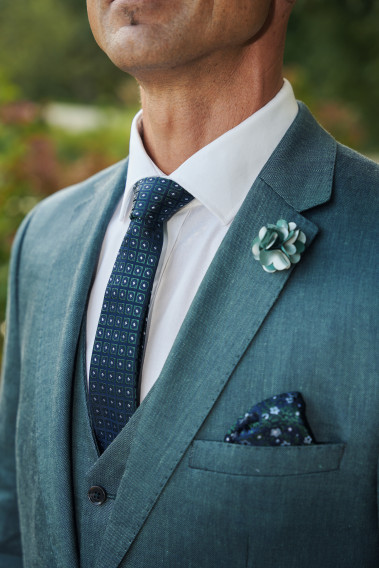 Costume SUAT vert. Plan sur la cravate bleu foncé et vert, la poche à motif floral ainsi qu'un pins fleur vert.
