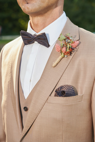Costume SUAT beige foncé. Nœud papillon et poche à motif bleu foncé et pins bouquet de fleur.
