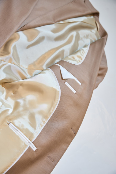 Zoom sur l’intérieur de la veste de costume SUAT couleur beige foncé. La doublure est beige et  comporte 3 poches intérieures.