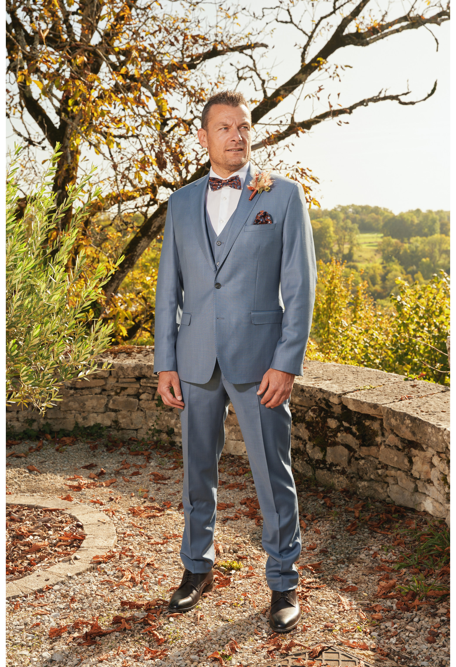 Homme de profil en costume SUAT couleur bleu orage 3 pièces dans une cours.