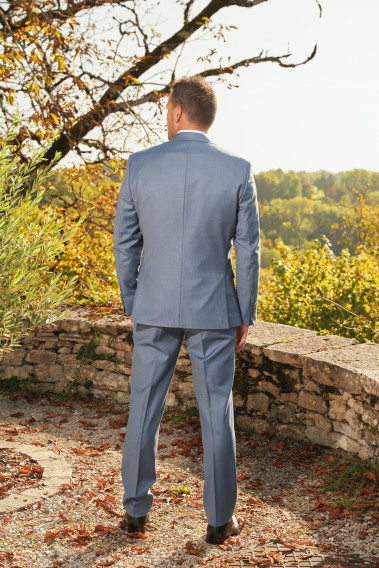 Homme de profil en costume SUAT couleur bleu orage 3 pièces dans une cours. Il porte des chaussures noires.