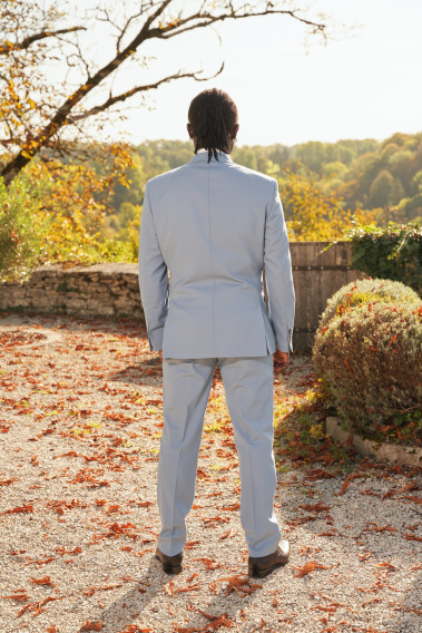 Homme de dos en costume SUAT couleur bleu grisé dans une cours. Il porte des chaussures noirs.