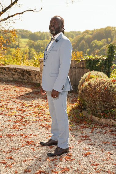Homme de profil en costume SUAT couleur bleu grisé dans une cours. Il porte des chaussures noirs.