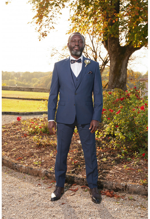 Homme de face en costume SUAT couleur marine à carreaux 3 pièces dans un jardin.