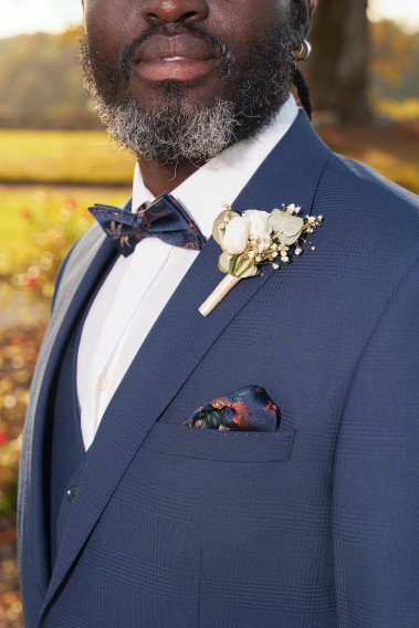 Costume SUAT couleur marine à carreaux . Plan sur le nœuds papillon à motif florale et son mouchoir de poche ainsi qu'un pins.