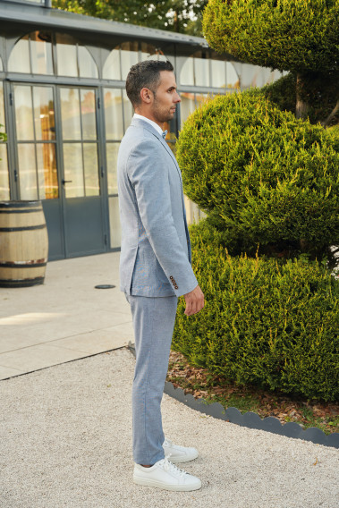 Homme de profil portant la veste TROPICALW bleue. Elle comporte une poche poitrine et 2 poches plaquées.