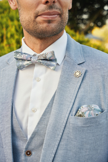 Zoom sur la veste TROPICALW bleue. L'homme porte une nœuds papillon et une mouchoir de poche.